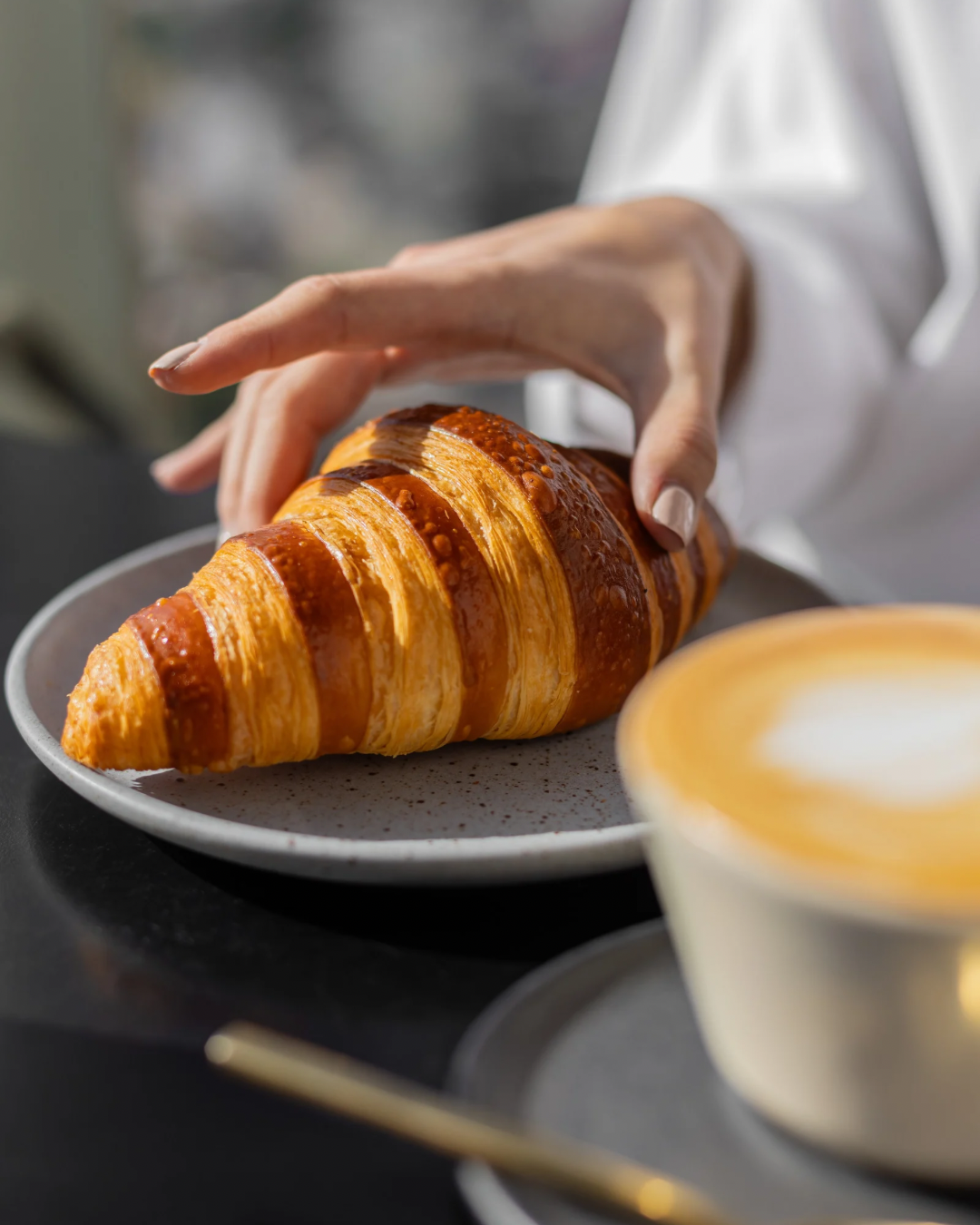 mujer comiendo croissant con café